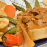 Senegalese chicken mafé: chicken pieces in a rich peanut sauce served over white rice with okra, cabbage, carrot and a whole Scotch bonnet pepper