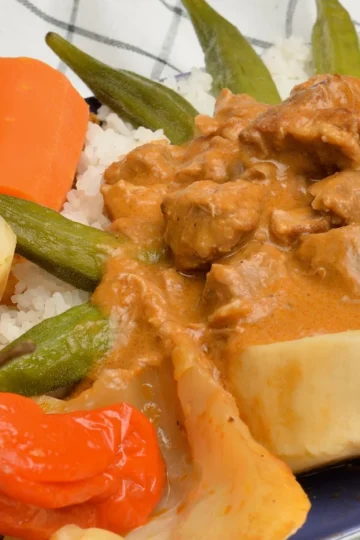 Senegalese chicken mafé: chicken pieces in a rich peanut sauce served over white rice with okra, cabbage, carrot and a whole Scotch bonnet pepper