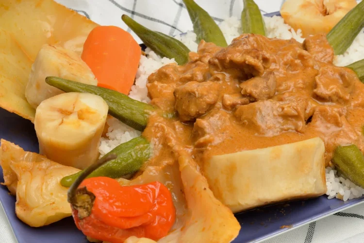 Senegalese chicken mafé: chicken pieces in a rich peanut sauce served over white rice with okra, cabbage, carrot and a whole Scotch bonnet pepper